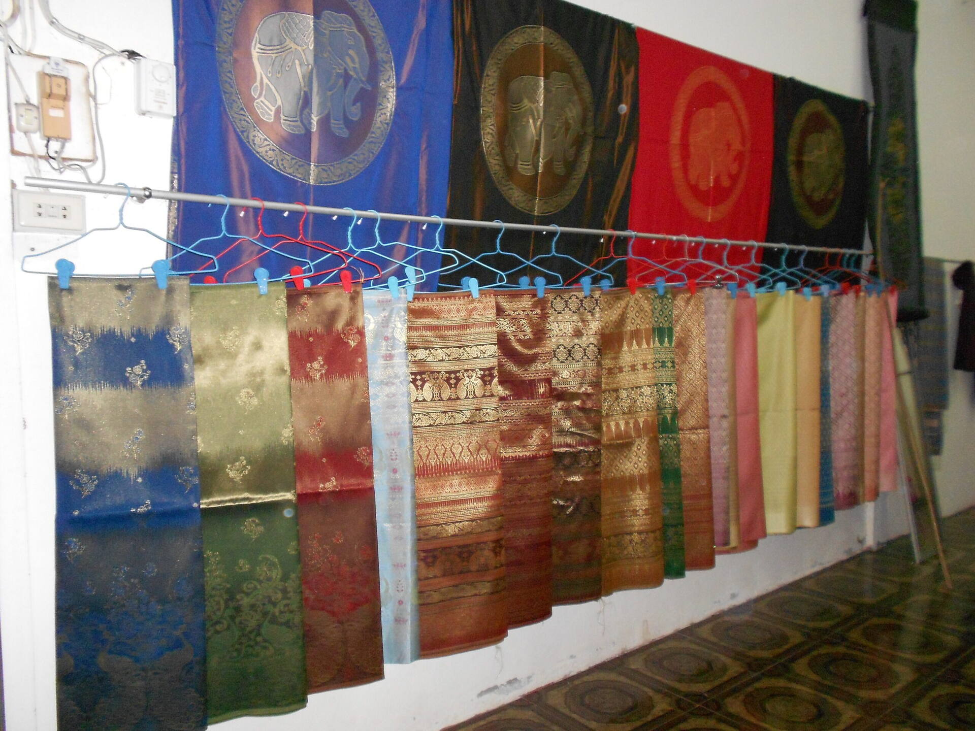 Colourful silk fabrics and gold brocade elephant panels hanging on display at Ban Tha Sawang, Surin province