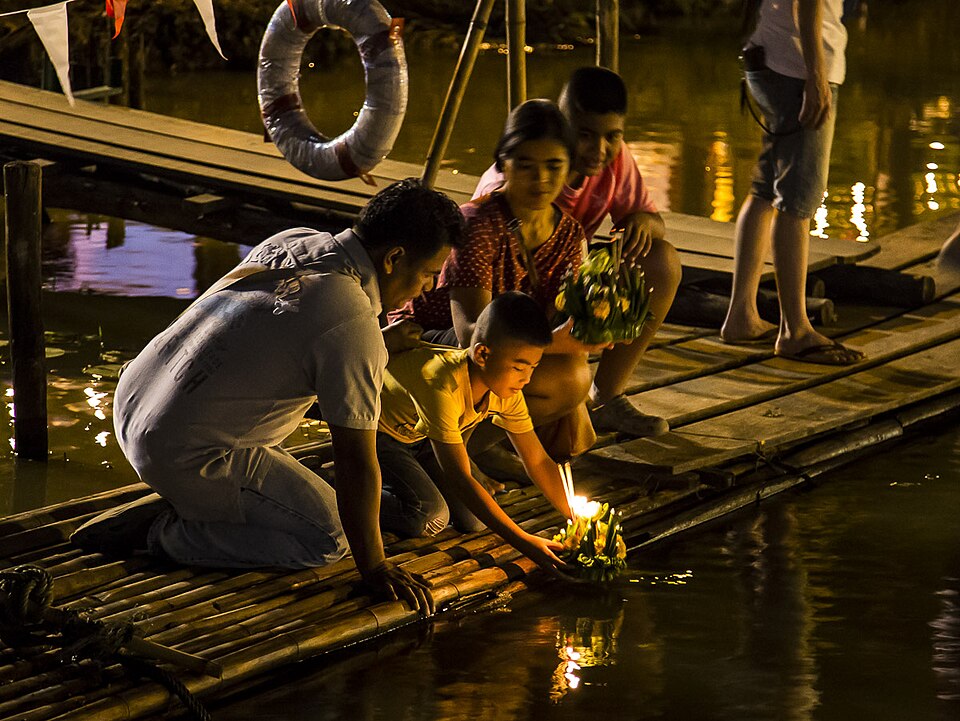 Thai people floating candle-lit krathongs on a river at night during Loy Krathong festival